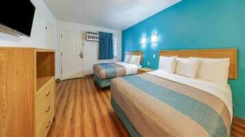 Habitación de hotel con dos camas, un armario de madera, un televisor y una puerta con cortina.