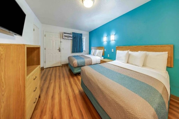 A hotel room with two beds, a wooden wardrobe, a television, and a door with a curtain.