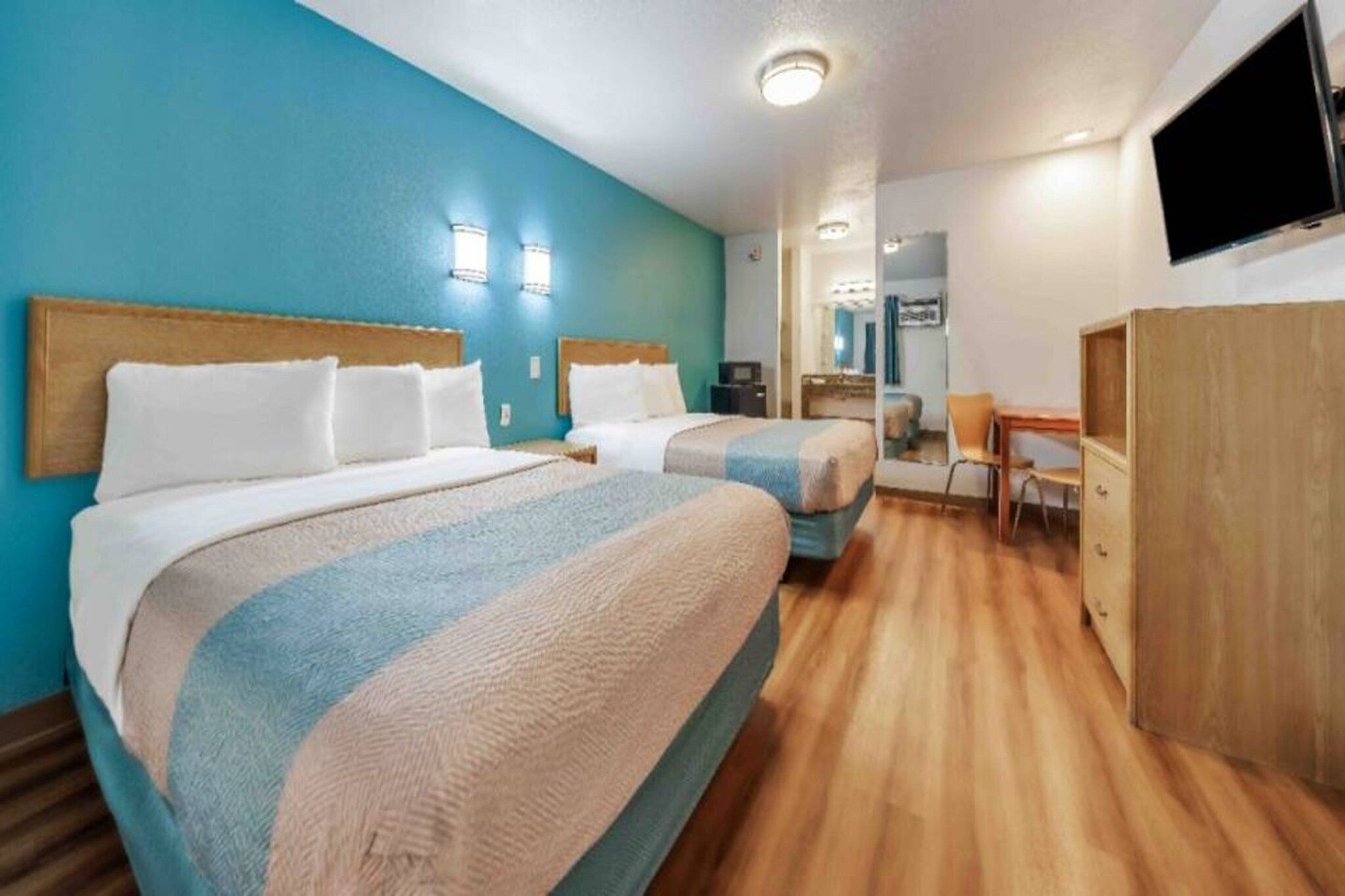 A hotel room with two beds, a desk, a chair, and a TV.