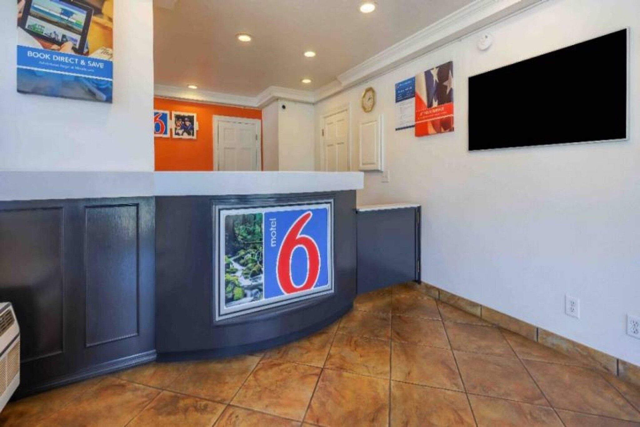 A hotel lobby with a reception desk, a clock, and a television screen.