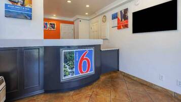 A hotel lobby with a reception desk, a clock, and a television screen.