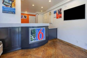 A hotel lobby with a reception desk, a clock, and a television screen.