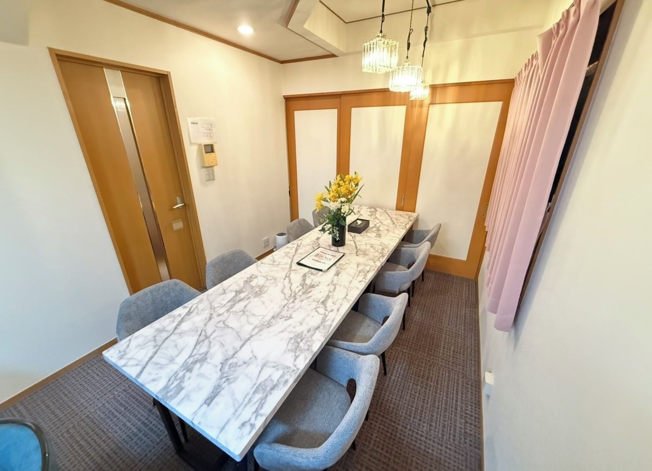 A conference room with a marble table, grey chairs, a vase with flowers, and a chandelier.