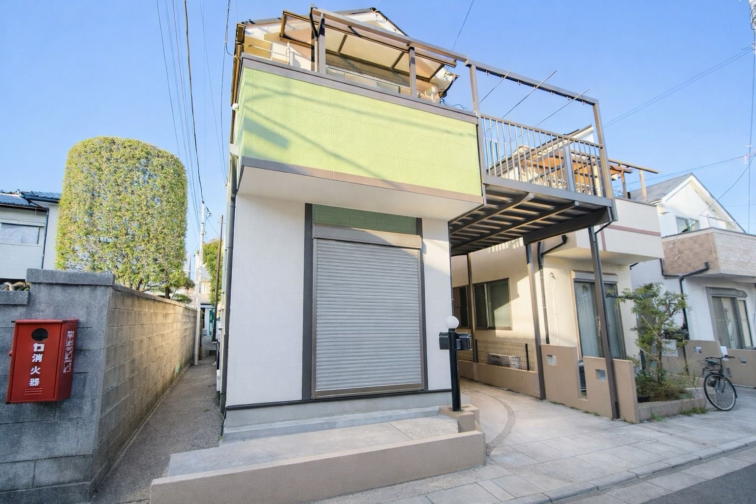 A modern two-story building with a green facade, a closed shutter, and a small balcony.