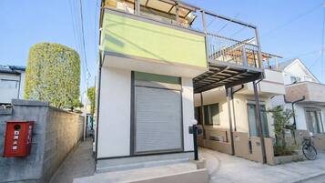 A modern two-story building with a green facade, a closed shutter, and a small balcony.