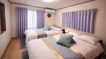 A hotel room with two beds, a clock on the wall, and a window with curtains.