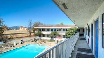 Un balcón de hotel con piscina, mobiliario exterior y vistas del entorno.