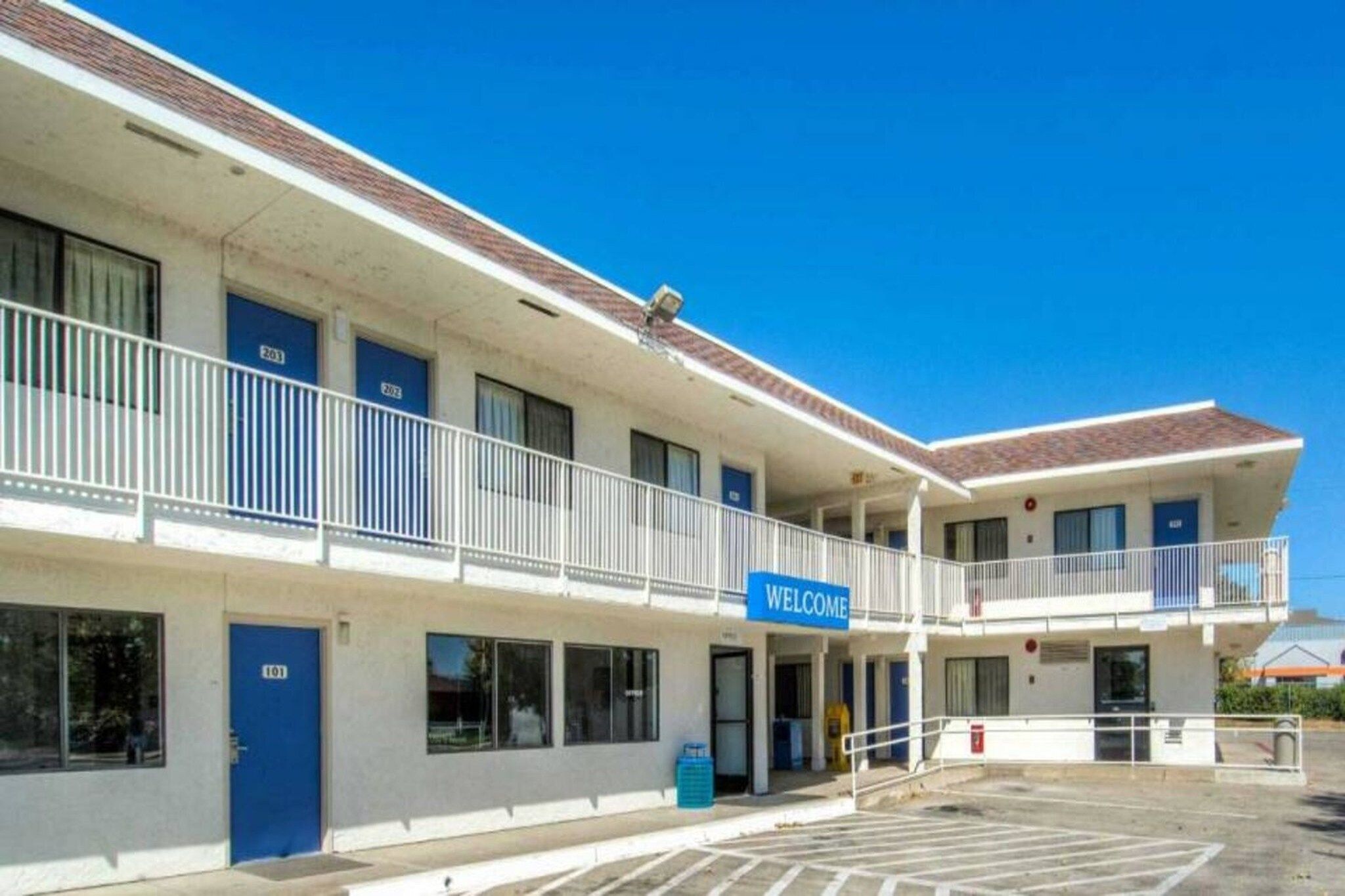 A two-story motel with a 'WELCOME' sign, numbered rooms, and a parking lot.