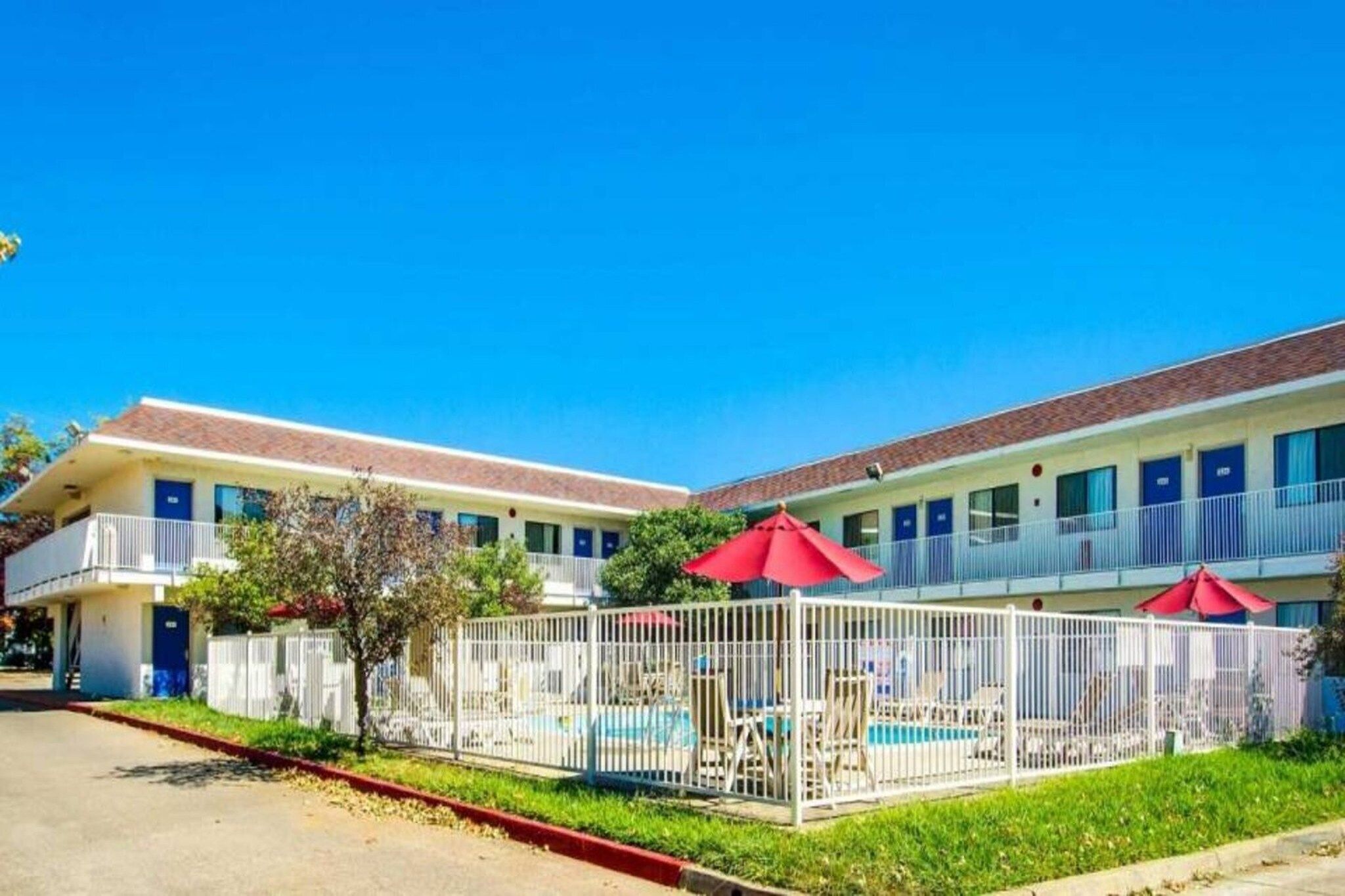 Un motel con piscina, área vallada y sombrillas rojas.