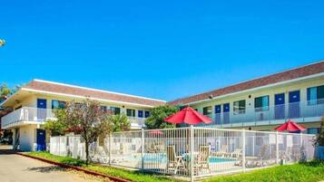 Un motel con piscina, área vallada y sombrillas rojas.
