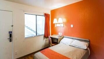 A hotel room with a bed, a desk, a chair, a window with a view of a staircase, and a door.