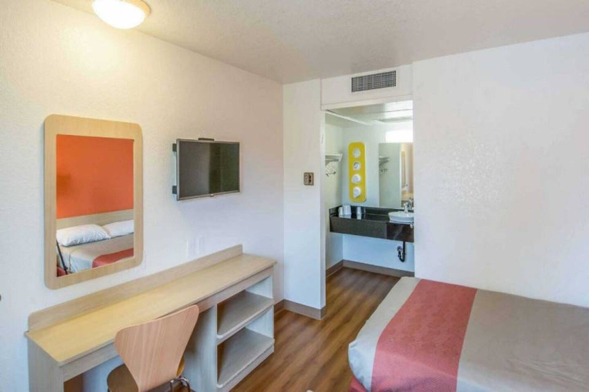 A compact hotel room with a bed, a desk, a chair, a television, and a bathroom visible through an open door.