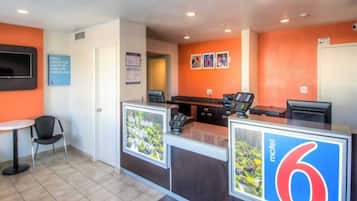 Una recepción de motel con mostrador, sillas y una pequeña mesa.