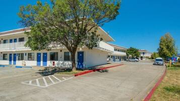 A motel with a parking lot, a tree in front, and a clear blue sky.