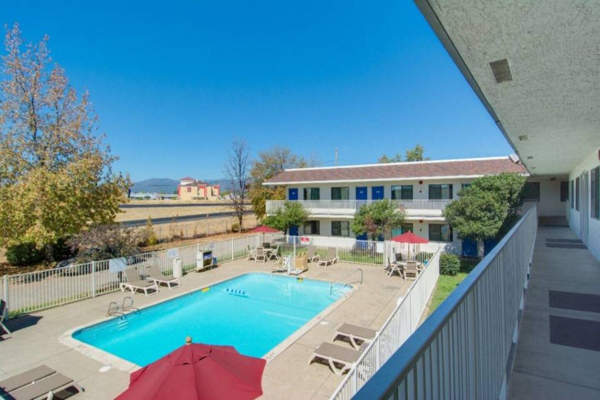 A hotel with a swimming pool, outdoor seating, and a view of the surrounding landscape.