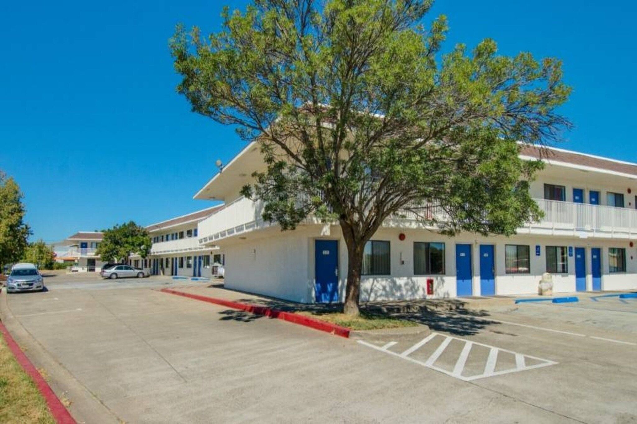 Un hotel con estacionamiento, un árbol en primer plano y un cielo azul despejado.