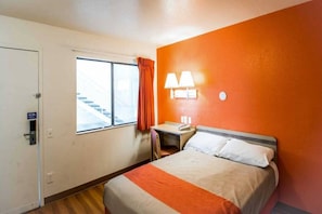 Una habitación de hotel con cama, escritorio, silla, ventana con vista a una escalera y una puerta.