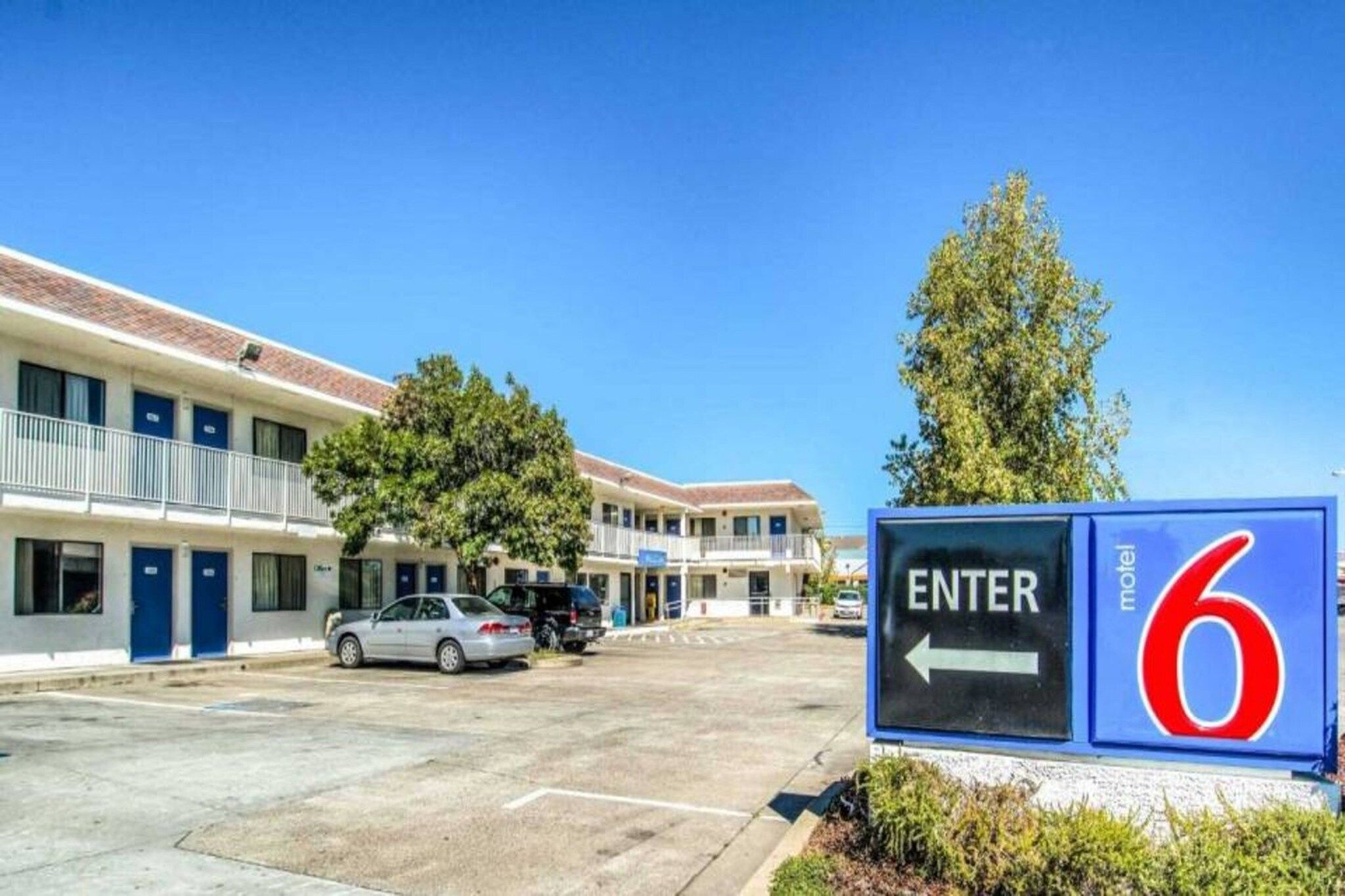 A motel with a clear entrance sign, a parking lot with cars, and a building with multiple doors and windows.