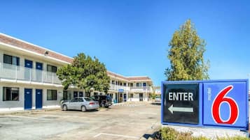 A motel with a clear entrance sign, a parking lot with cars, and a building with multiple doors and windows.