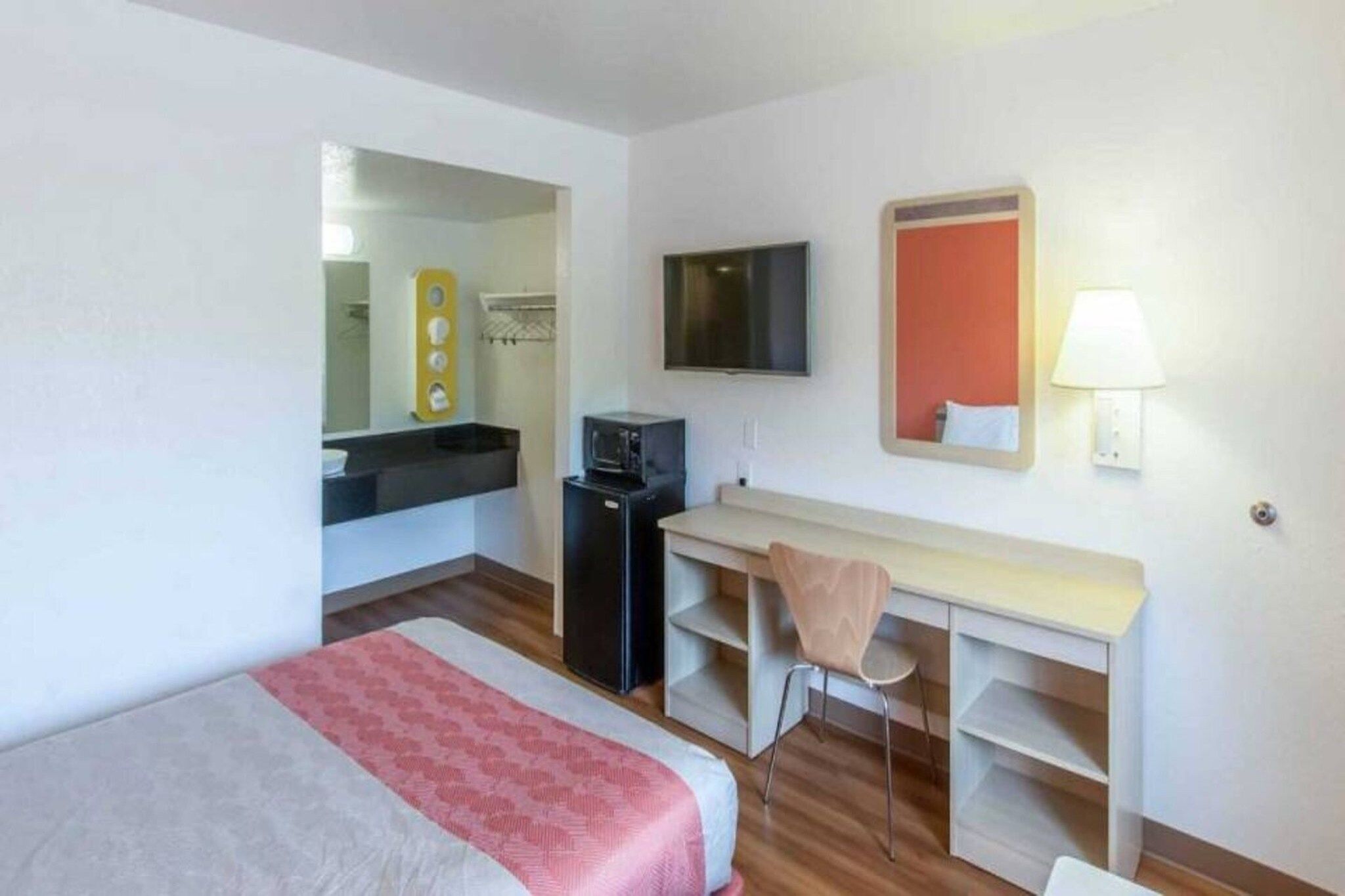 A hotel room with a bed, a desk with a chair, a television, and a mirror.
