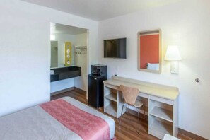 Hotellihuone, jossa on sänky, työpöytä tuolilla, televisio ja peili.