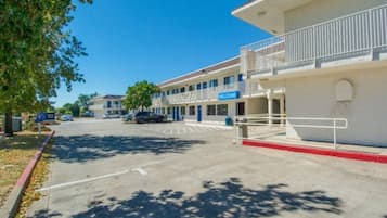 Un motel de varios pisos con un cartel que dice 'WELCOME', un estacionamiento y un cielo azul despejado.