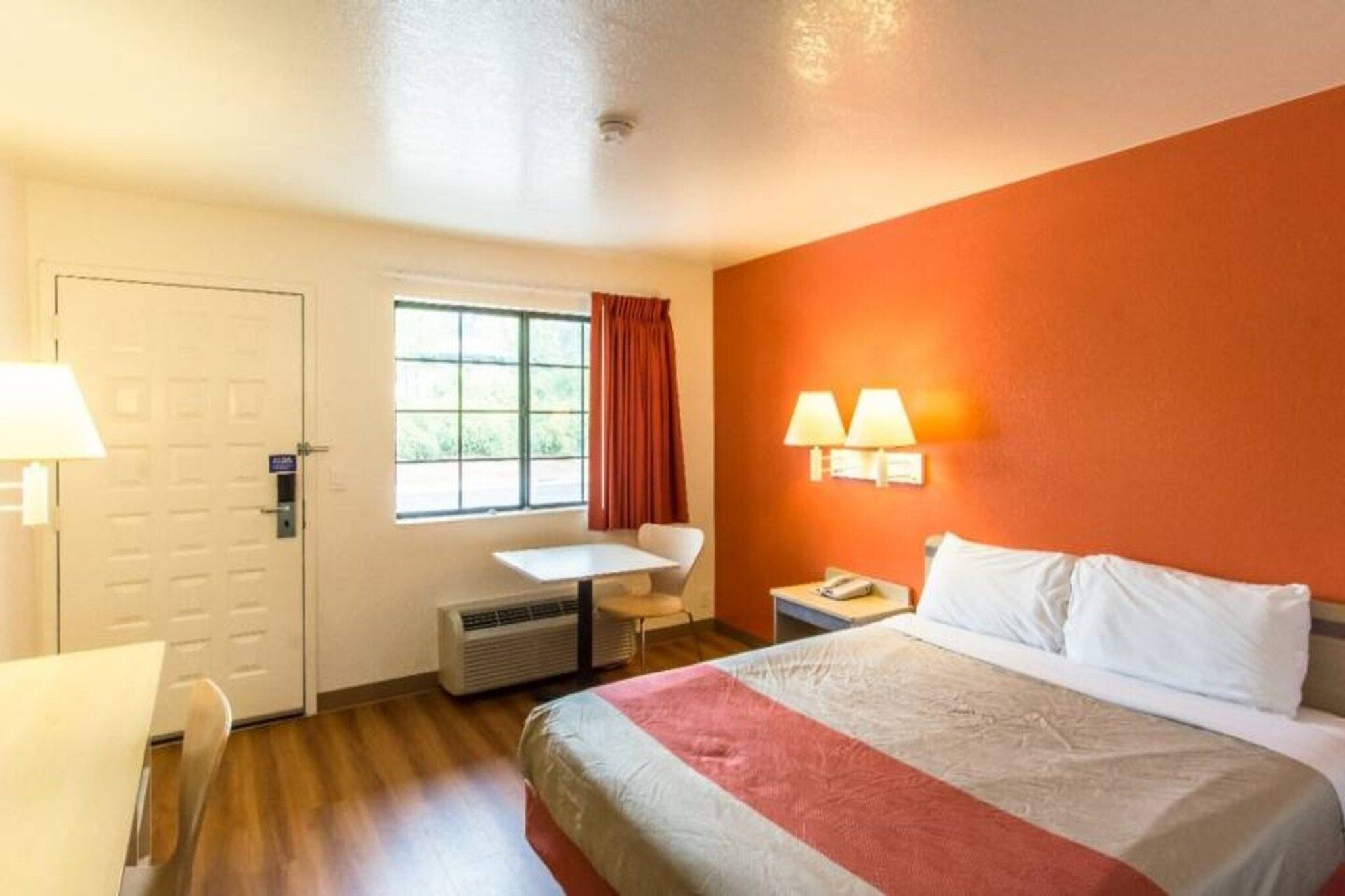 Habitación de hotel con cama, escritorio, silla, ventana con cortinas y dos lámparas de pared.