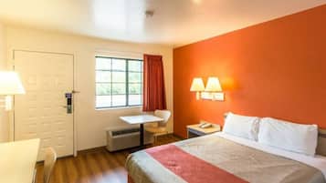 Habitación de hotel con cama, escritorio, silla, ventana con cortinas y dos lámparas de pared.