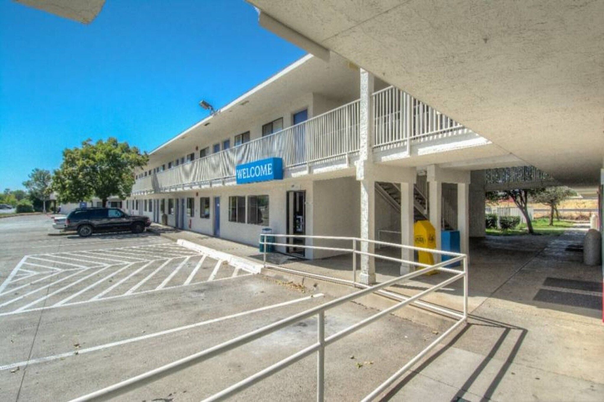 A motel with a 'WELCOME' sign, a covered parking area, and a building with multiple windows.
