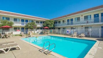 A hotel with a swimming pool, outdoor seating, and a fenced area.