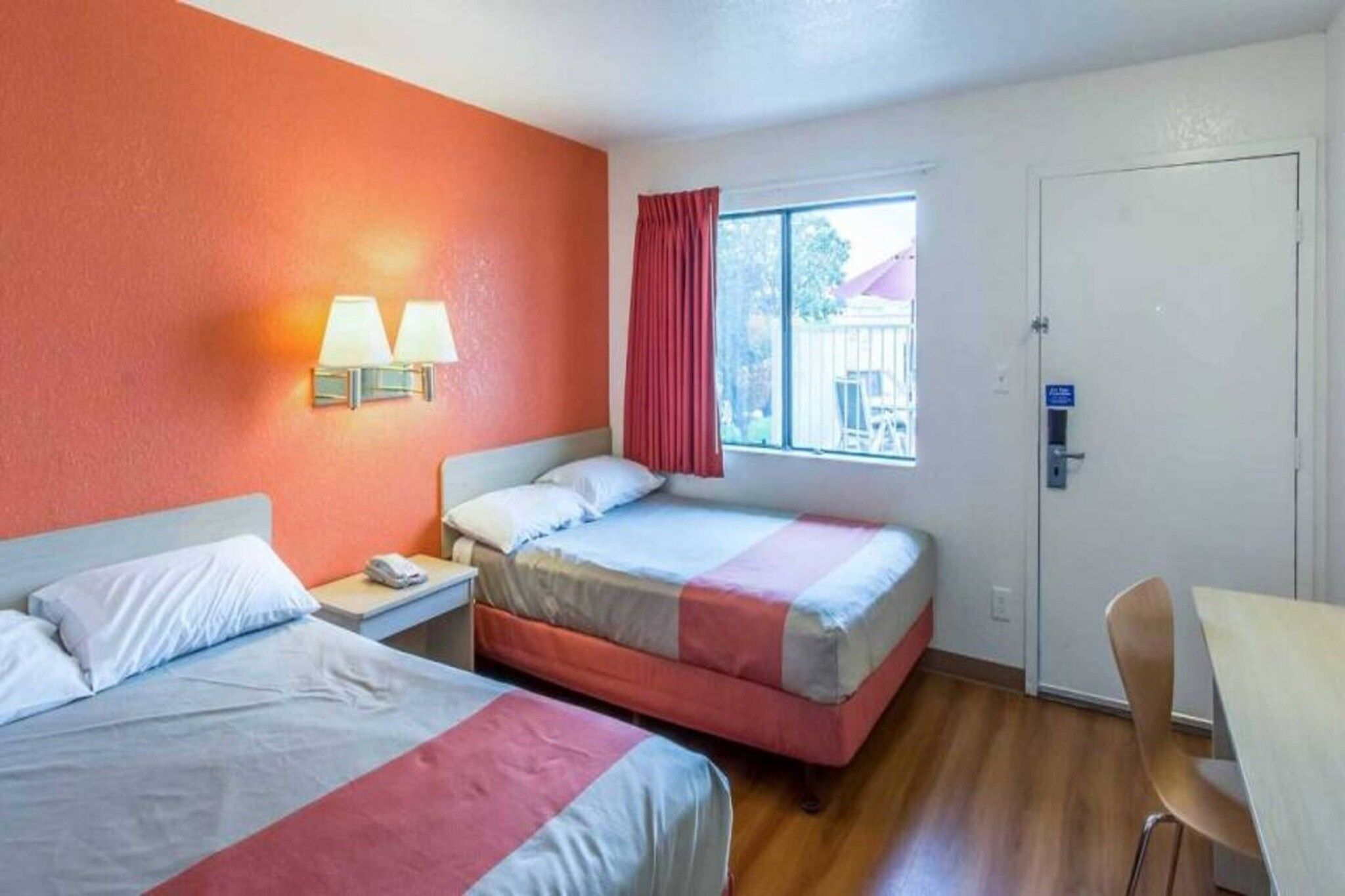 Une chambre d’hôtel avec deux lits, une fenêtre avec des rideaux rouges, un bureau et une chaise.