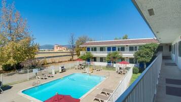 A hotel with a swimming pool, outdoor seating, and a view of the surrounding landscape.