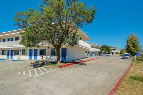 Un motel con estacionamiento, un árbol en primer plano y un cielo azul despejado.