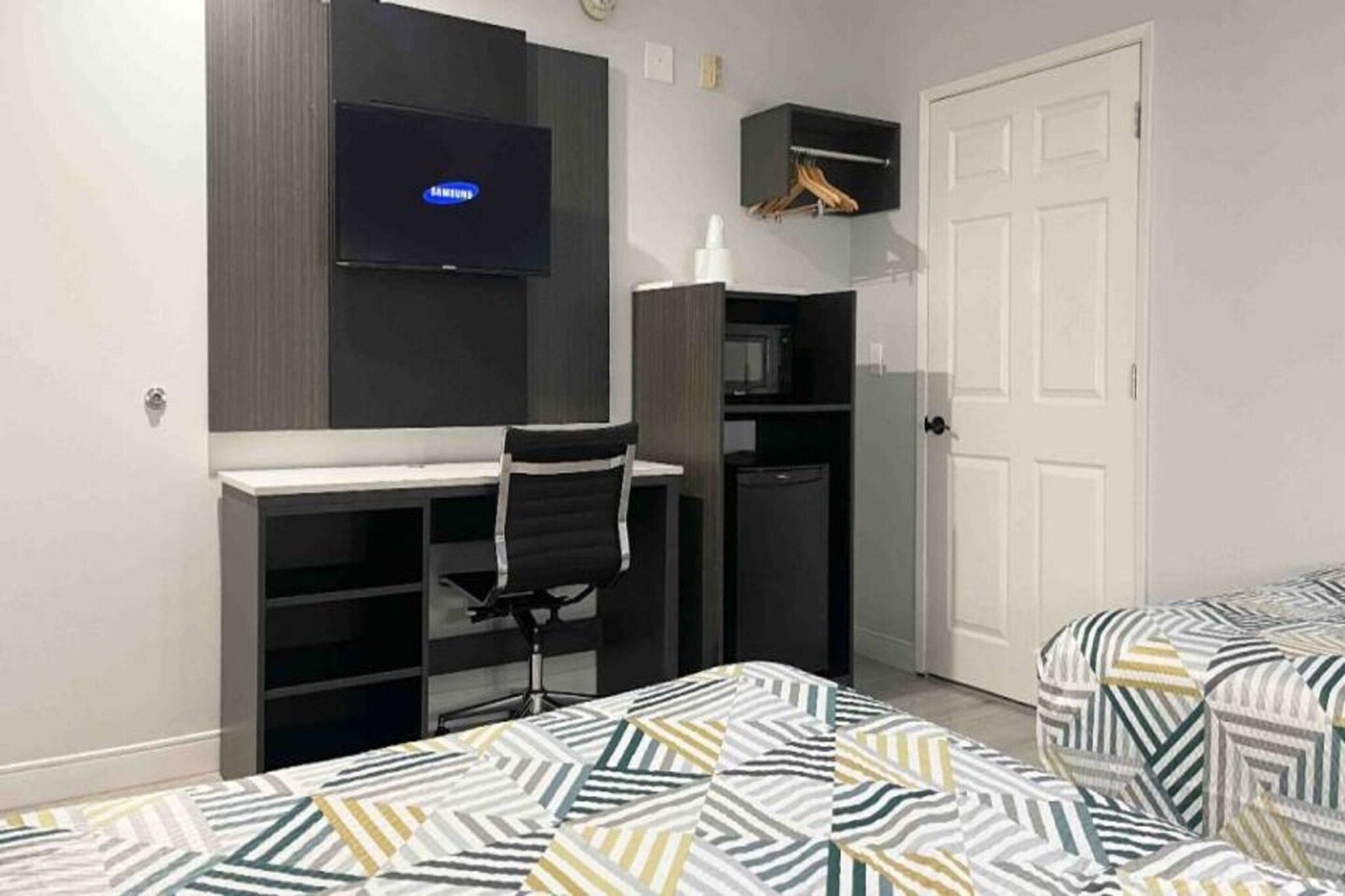 Een slaapkamer met een bureau, een stoel, een televisie, een kledingkast en twee bedden met beddengoed met een patroon.