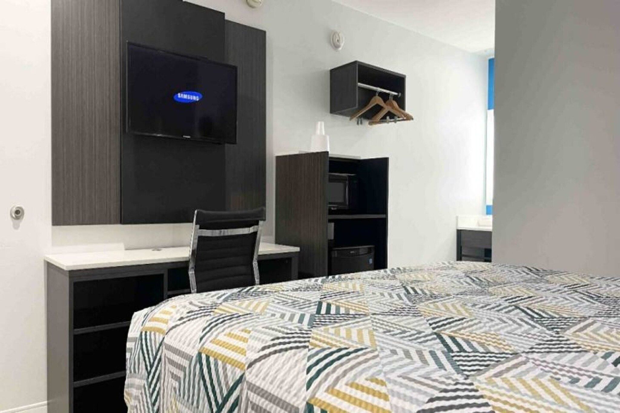 A hotel room with a bed, a desk, a chair, a television, and a wardrobe.