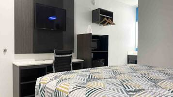 A hotel room with a bed, a desk, a chair, a television, and a wardrobe.