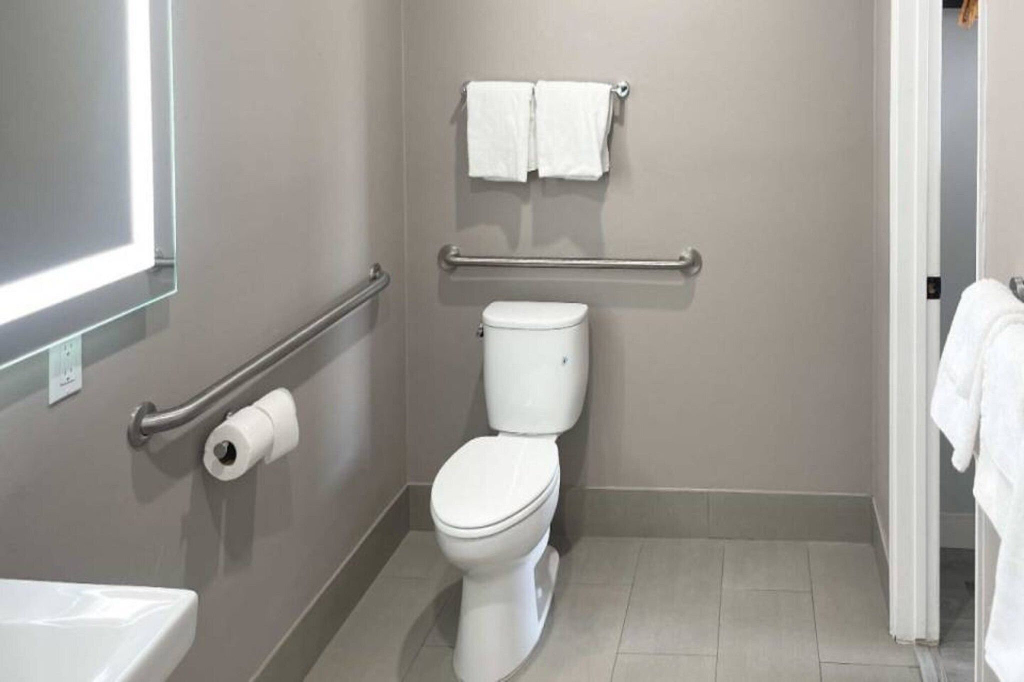 A bathroom with a toilet, a handrail, a towel rack, and a toilet paper holder.