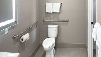 A bathroom with a toilet, a handrail, a towel rack, and a toilet paper holder.