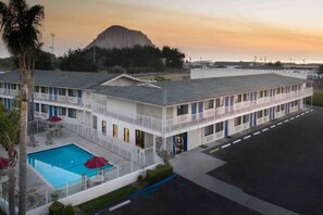A motel with a swimming pool, a mountain in the background, and a parking lot. - King Bed | ADA/RI Shower/Micfridge (Morro Bay)