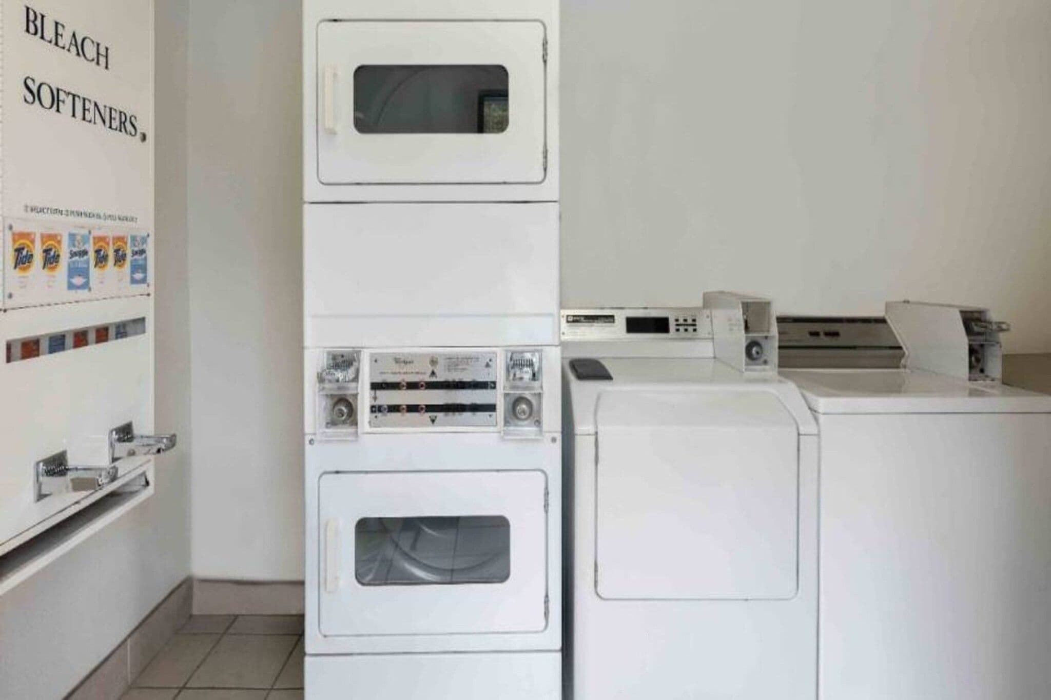A laundry area with stacked washing machines and dryers, a wall-mounted washing machine, and a shelf with detergent bottles.