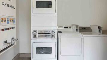 A laundry area with stacked washing machines and dryers, a wall-mounted washing machine, and a shelf with detergent bottles.