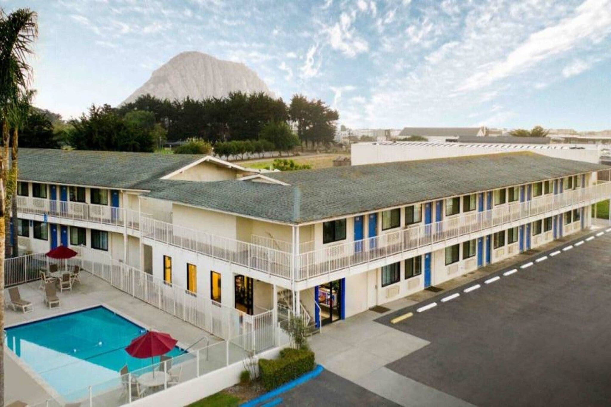 A motel with a swimming pool, multiple balconies, and a mountain in the background.
