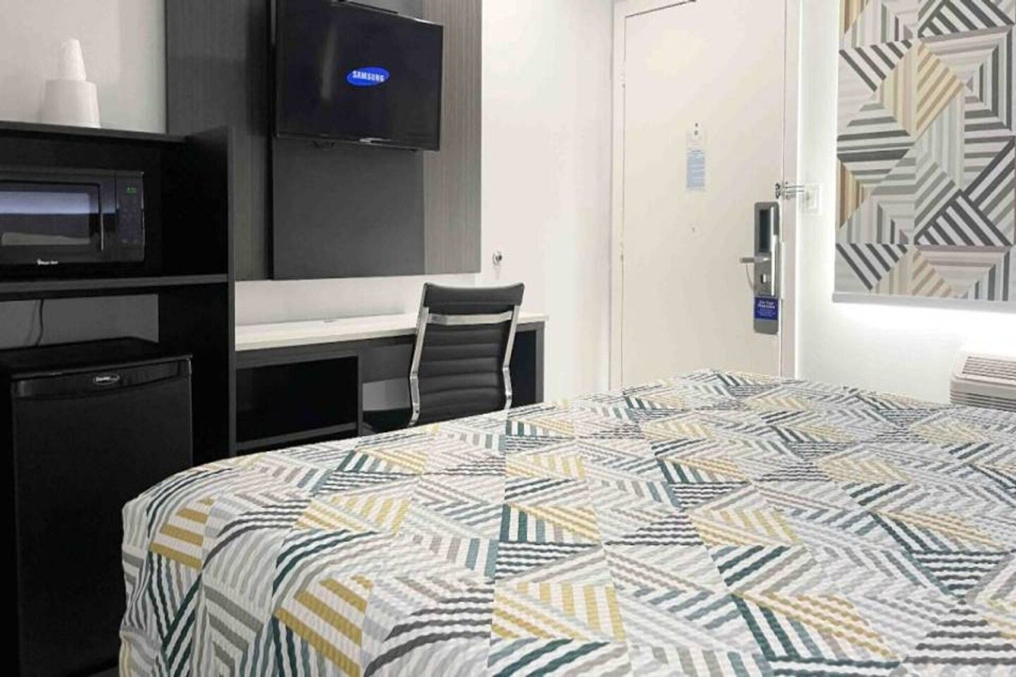 Hotellihuone, jossa on sänky, työpöytä, tuoli, televisio ja ovi.