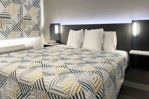 A hotel room with a large bed, a bedside table, a nightstand, and a patterned wall. - Spacious King Bed|Micfridge|Pool (Morro Bay)
