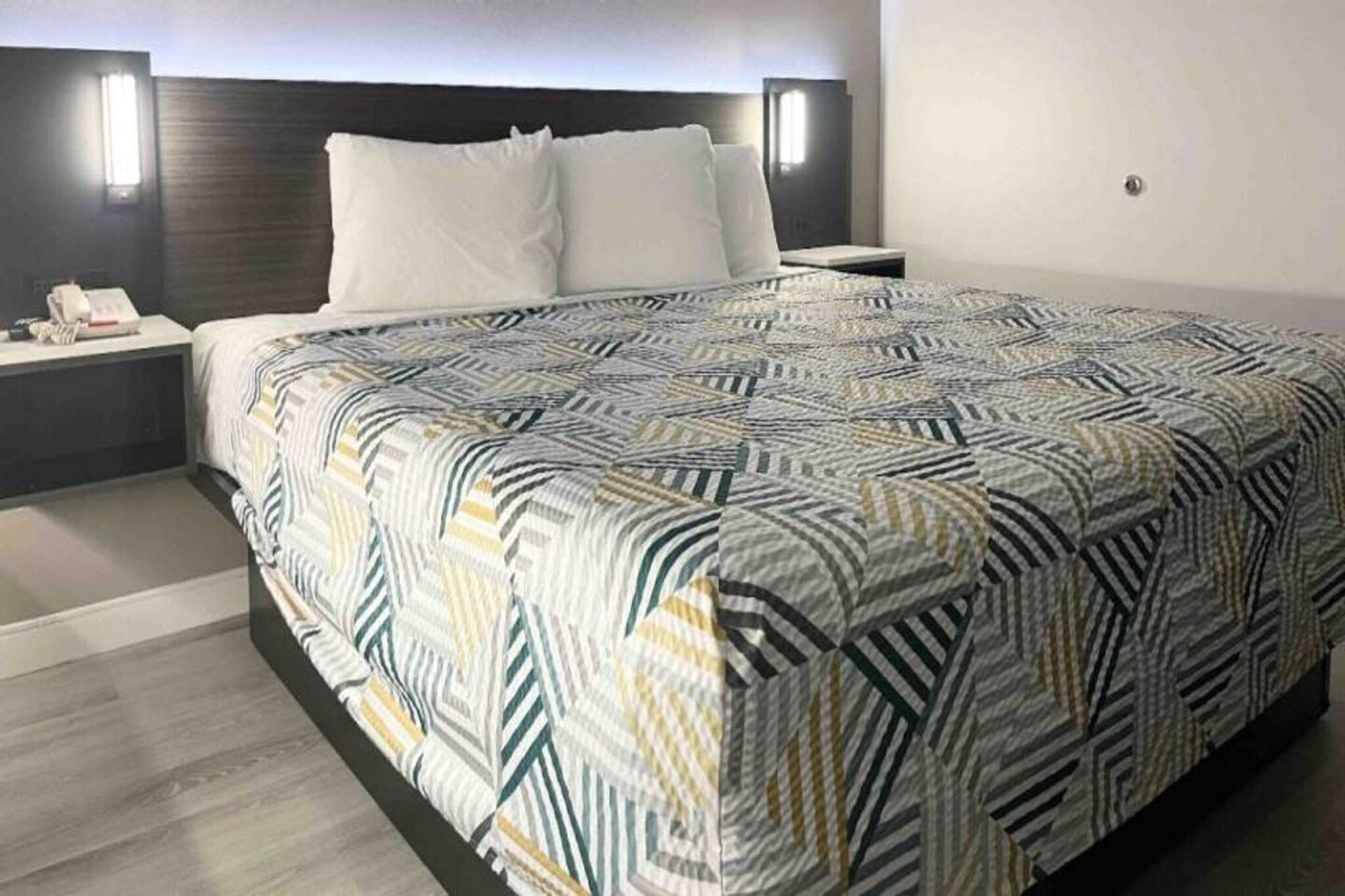 A hotel room with a large bed, a bedside table, and a nightstand.
