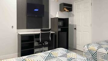 A bedroom with a desk, a chair, a TV, a wardrobe, and two beds with patterned bedding.