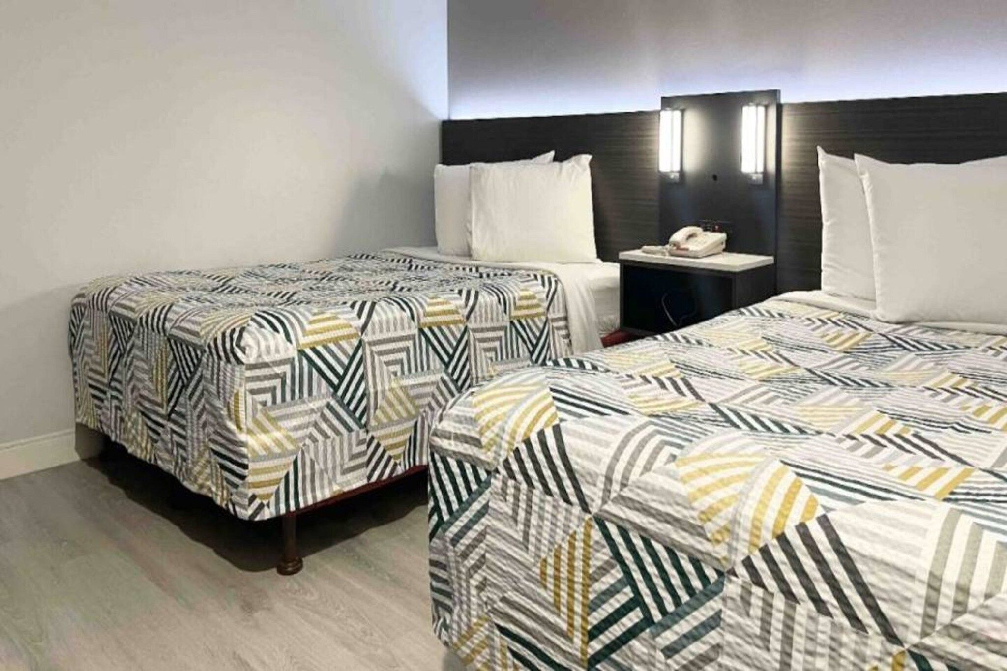 Hotellihuone, jossa on kaksi sänkyä, yöpöytä ja seinään kiinnitetty valaisin.