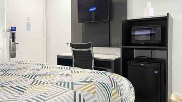 A hotel room with a bed, a desk, a chair, a television, and a microwave.
