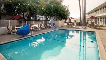 A swimming pool with lounge chairs and umbrellas, surrounded by a fence and trees.