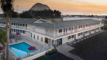 A motel with a swimming pool, a mountain in the background, and a parking lot.